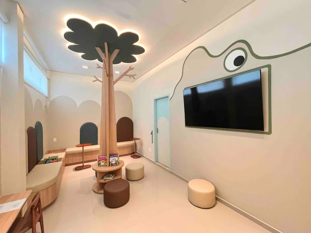 Sala de espera da recepção, com árvore de madeira, pufes e livros infantis