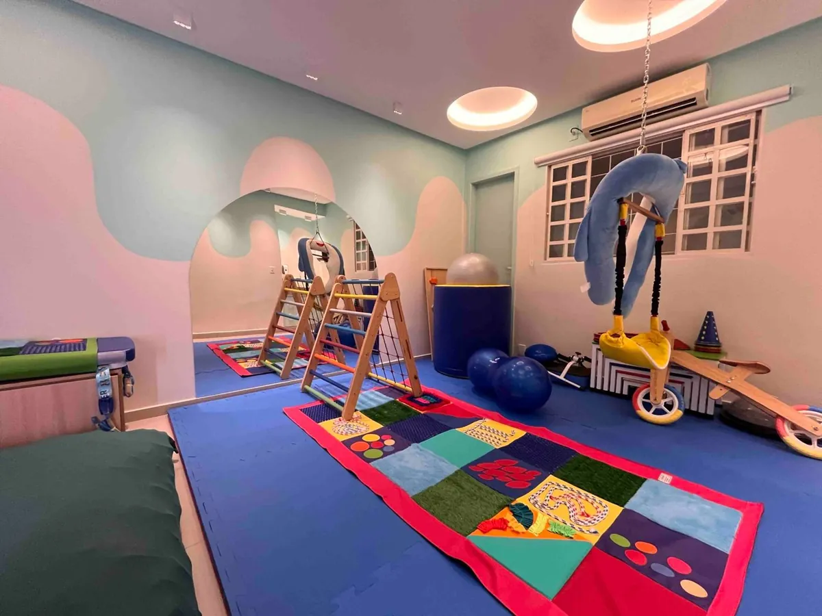 Sala sensorial com tatame colorido, triângulos de escalada e balanço