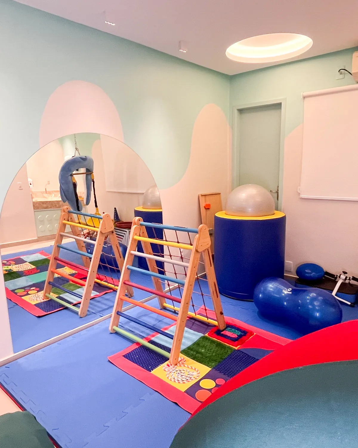 Triângulos de escalada de madeira, bola e tatame colorido na sala de psicomotricidade