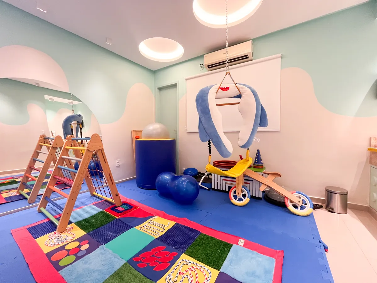 Sala de psicomotricidade com triângulos de escalada, bolas azuis, balanço e tatame colorido