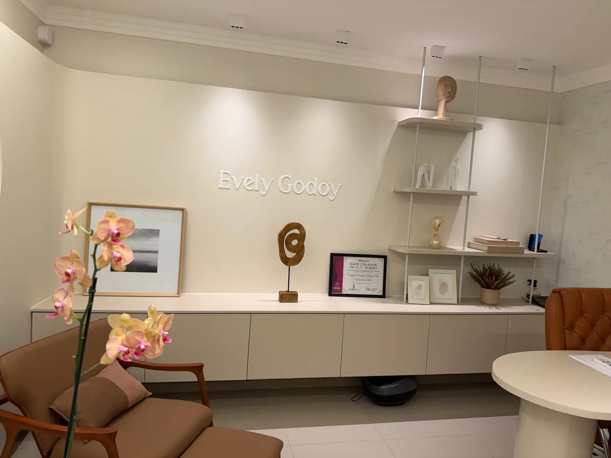 Poltrona e orquídea no consultório, com estante iluminada e quadros ao fundo