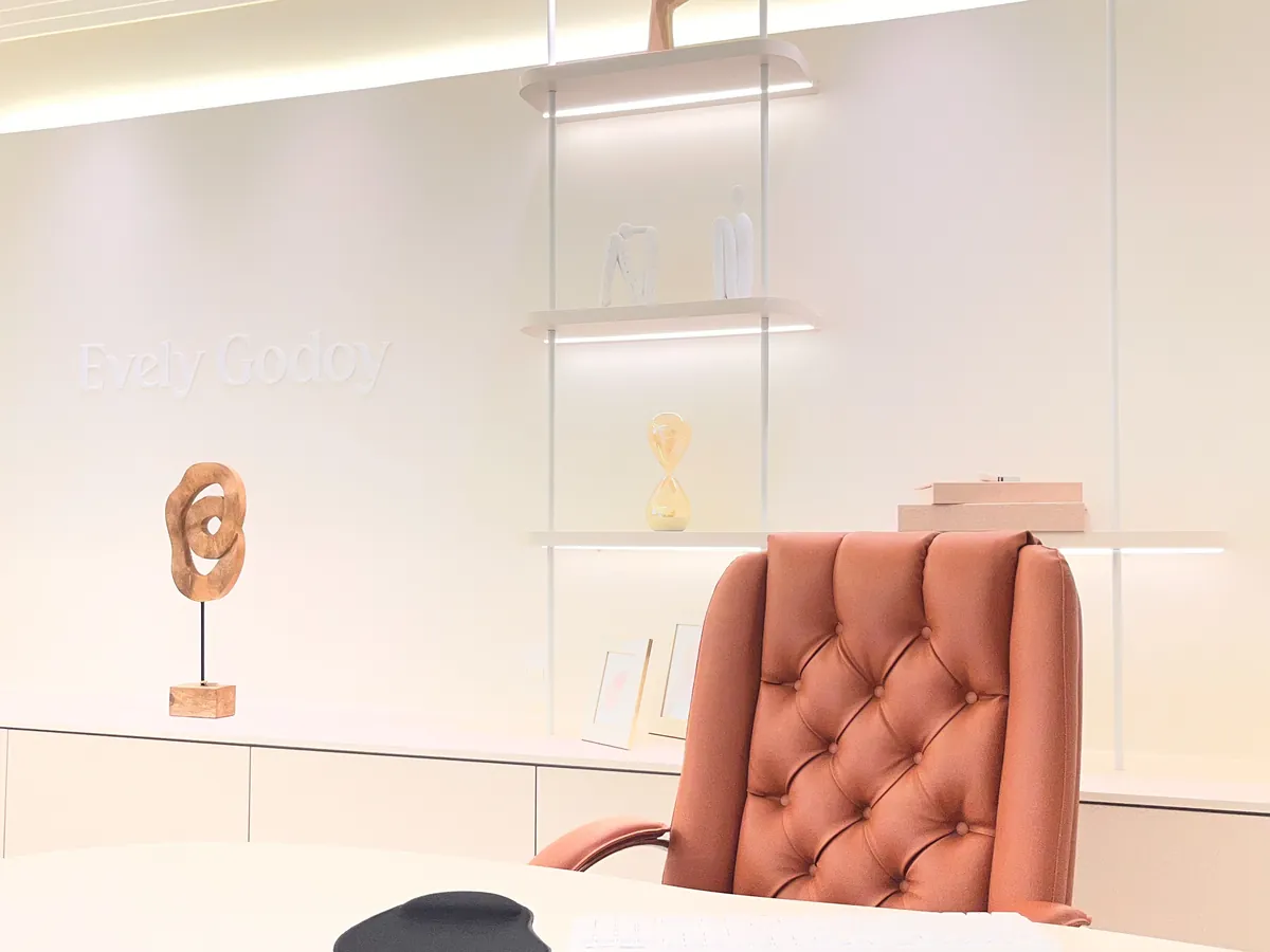 Mesa de atendimento com cadeira de couro, escultura e estante iluminada ao fundo