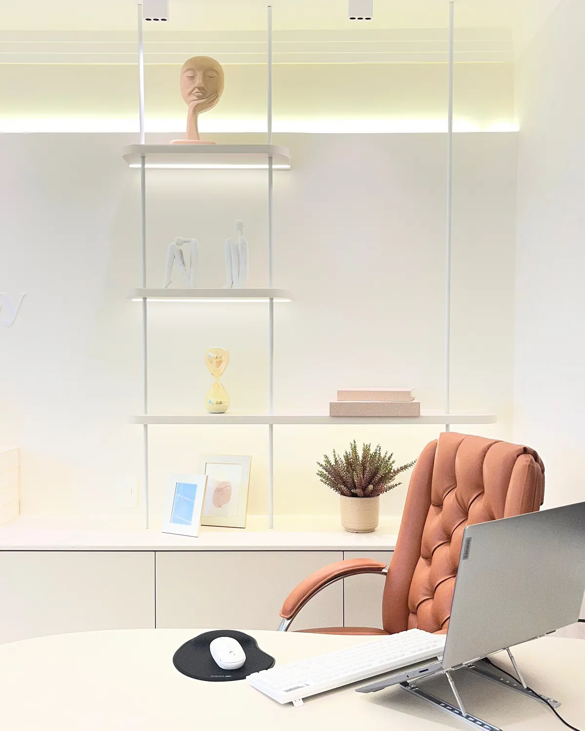 Mesa de trabalho com notebook no suporte, cadeira de couro e estante iluminada