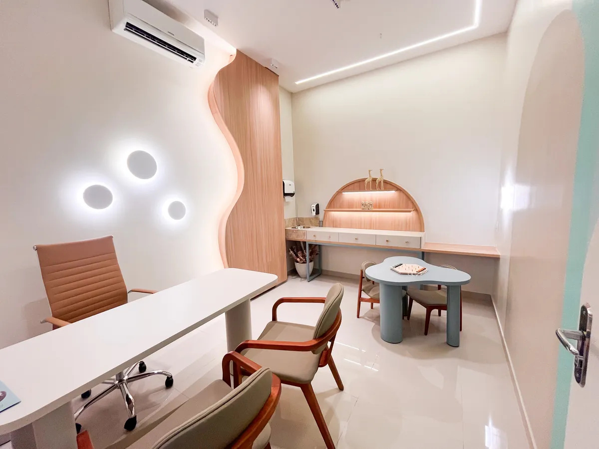 Consultório infantil com mesa de trabalho, cadeiras, mesinha em forma de nuvem e prateleira em arco ao fundo