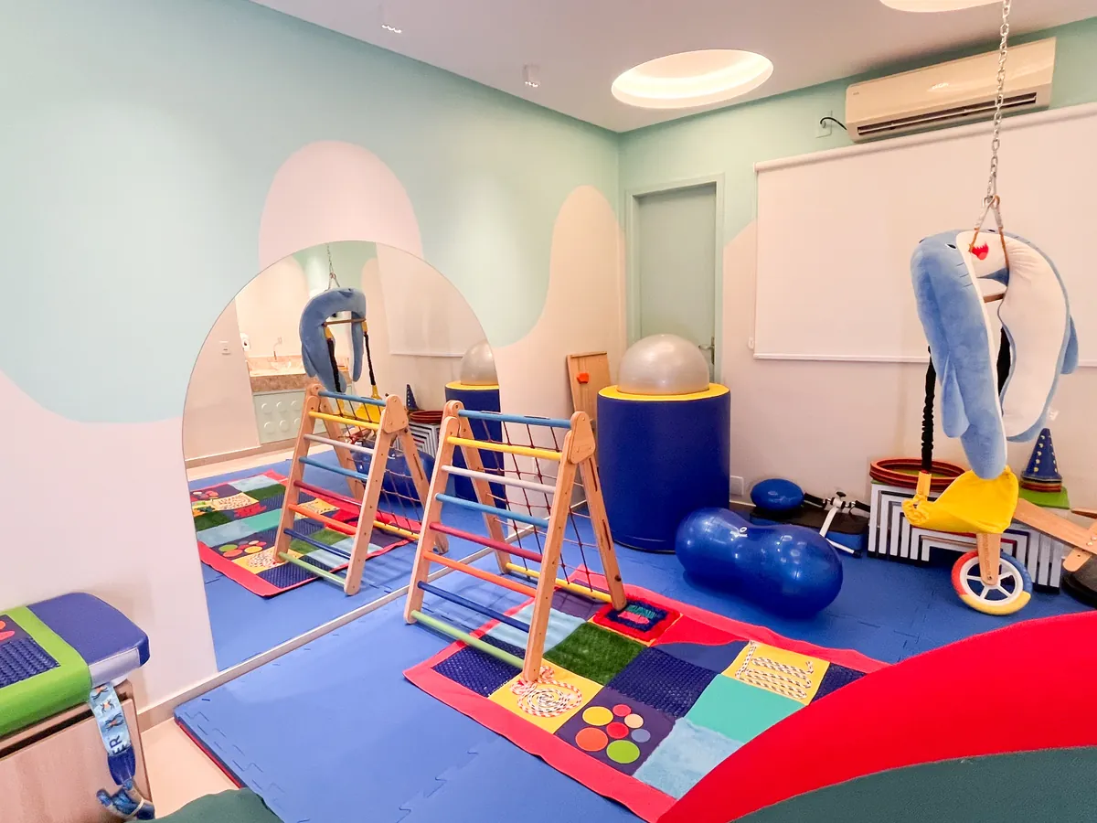 Sala sensorial com triângulos de escalada, bolas azuis, balanço de golfinho e tatame colorido