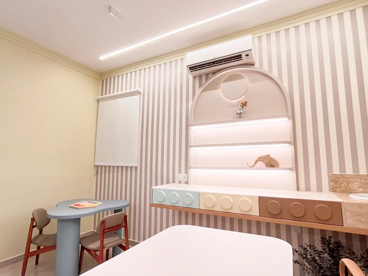 Consultório infantil com mesinha em forma de nuvem, cadeiras, bancada com gavetas e prateleiras iluminadas