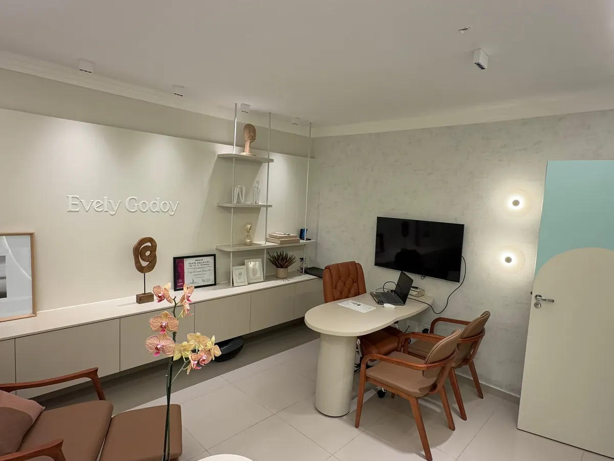 Consultório adulto visto da entrada, com poltrona, mesa de atendimento, cadeiras e estante